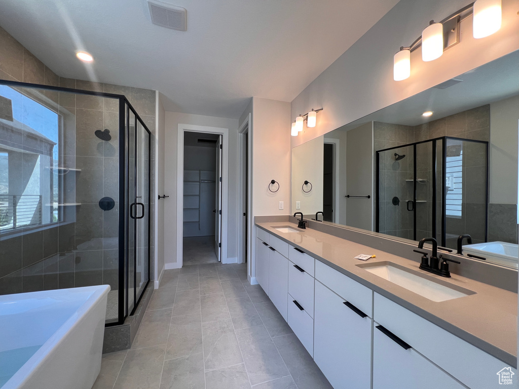 Bathroom featuring a stall shower, a freestanding tub, double vanity, tile patterned flooring, and recessed lighting