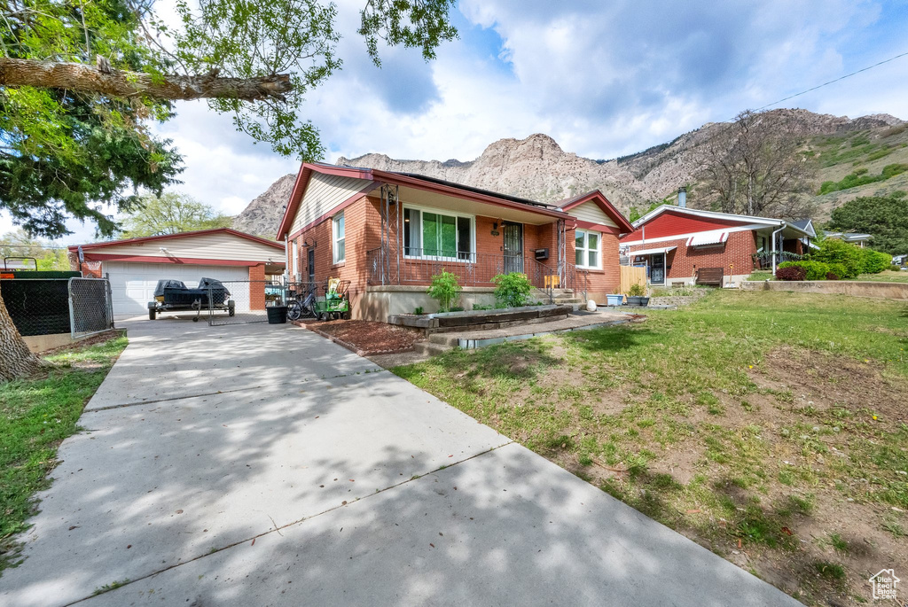 Single story home featuring brick siding, a garage, a front yard, an outbuilding, and a mountain view