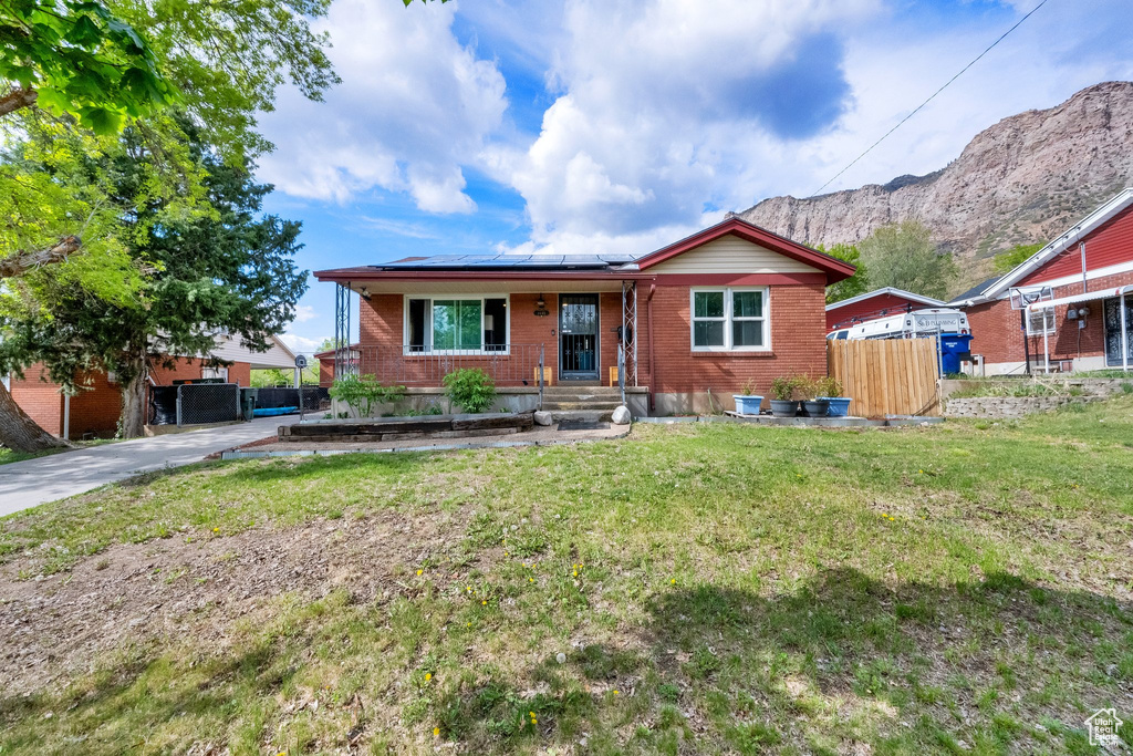 View of front of house featuring roof mounted solar panels, fence, a front lawn, and brick siding