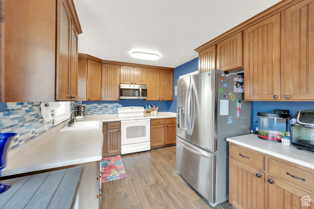 Kitchen featuring appliances with stainless steel finishes, a sink, light wood finished floors, light countertops, and decorative backsplash