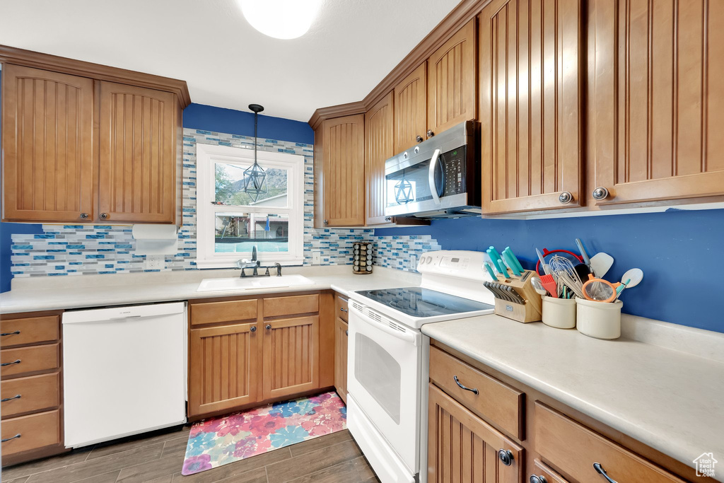 Kitchen featuring a sink, hanging light fixtures, backsplash, and white appliances