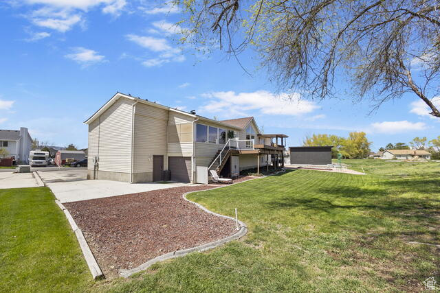 Back of house with stairs, a garage, a deck, a yard, and driveway