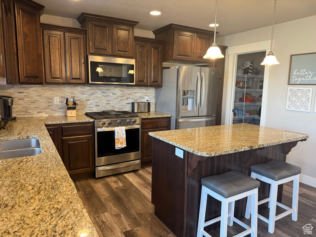 Kitchen featuring stainless steel appliances, dark wood finished floors, dark brown cabinetry, tasteful backsplash, and light stone counters
