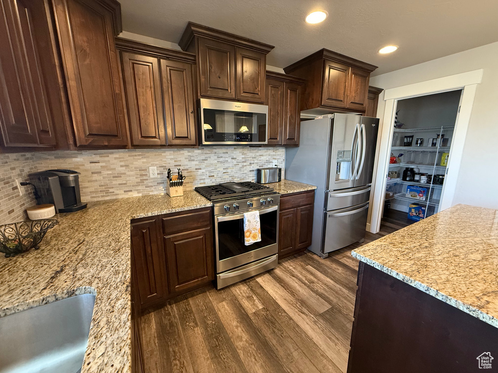 Kitchen with appliances with stainless steel finishes, dark wood-style floors, backsplash, dark brown cabinetry, and recessed lighting