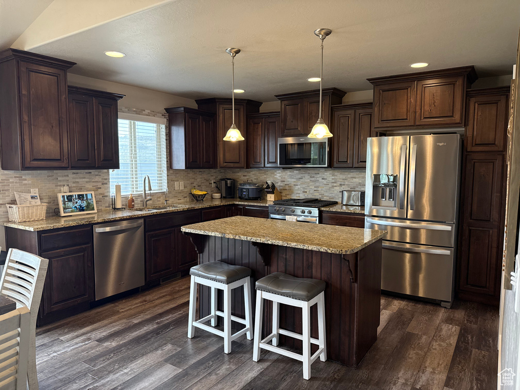 Kitchen with appliances with stainless steel finishes, a sink, dark brown cabinets, dark wood-style floors, and recessed lighting