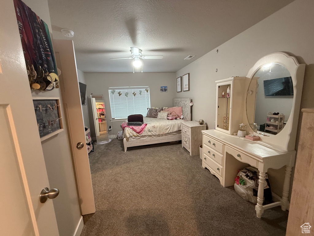 Carpeted bedroom featuring ceiling fan, a textured ceiling, and visible vents