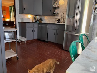 Kitchen featuring a sink, decorative backsplash, appliances with stainless steel finishes, gray cabinetry, and dark wood-type flooring