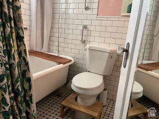 Full bathroom with tile patterned flooring, tile walls, toilet, and shower / bath combo