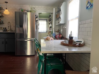 Kitchen featuring light countertops, dark wood-style floors, stainless steel fridge, and backsplash