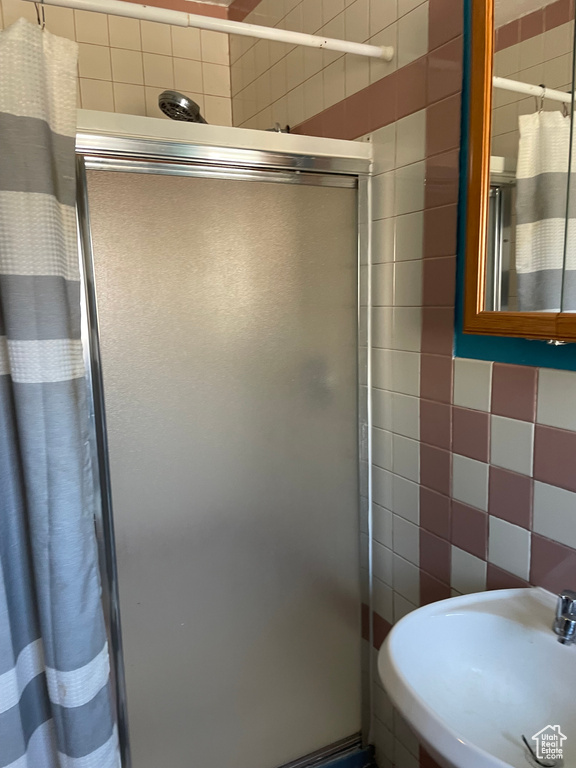 Full bath with tile walls, a sink, and a shower stall