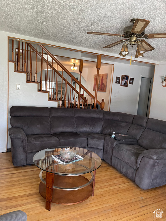 Living area with a textured ceiling, ceiling fan, stairway, and wood finished floors