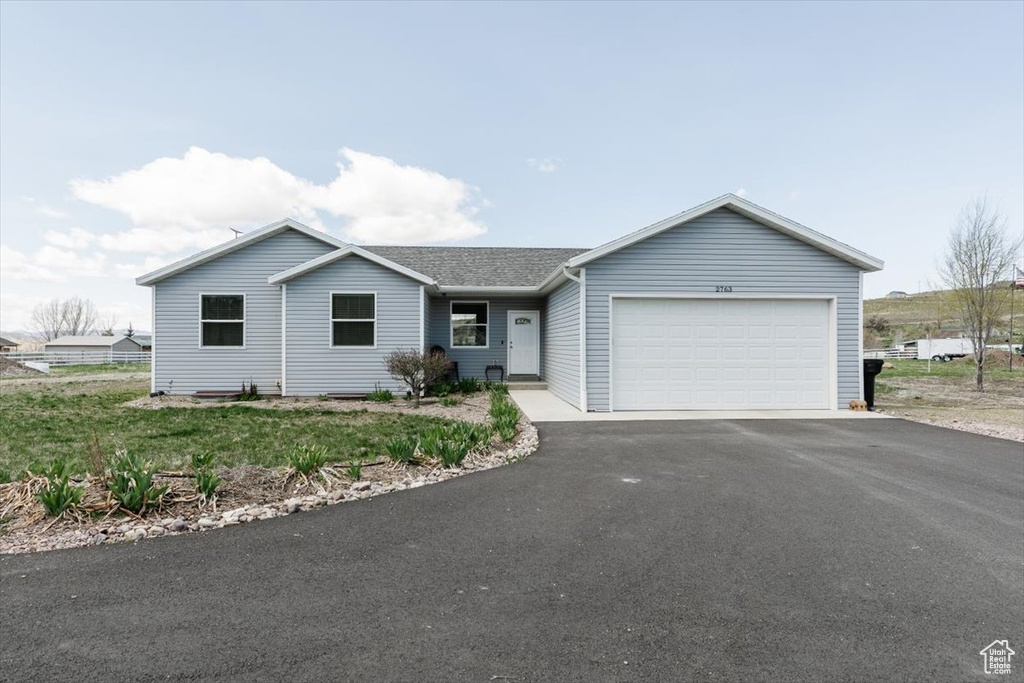 Ranch-style home featuring a shingled roof, aphalt driveway, and a garage