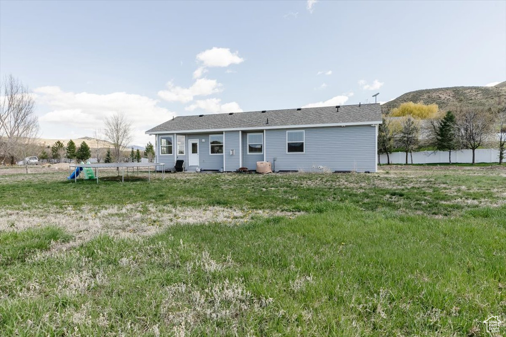 Rear view of house with fence, a trampoline, and a mountain view