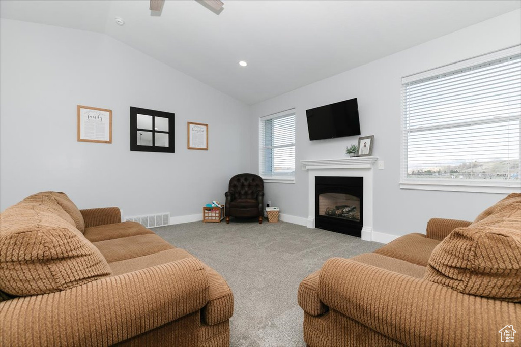 Carpeted living area featuring baseboards, lofted ceiling, a ceiling fan, and a fireplace