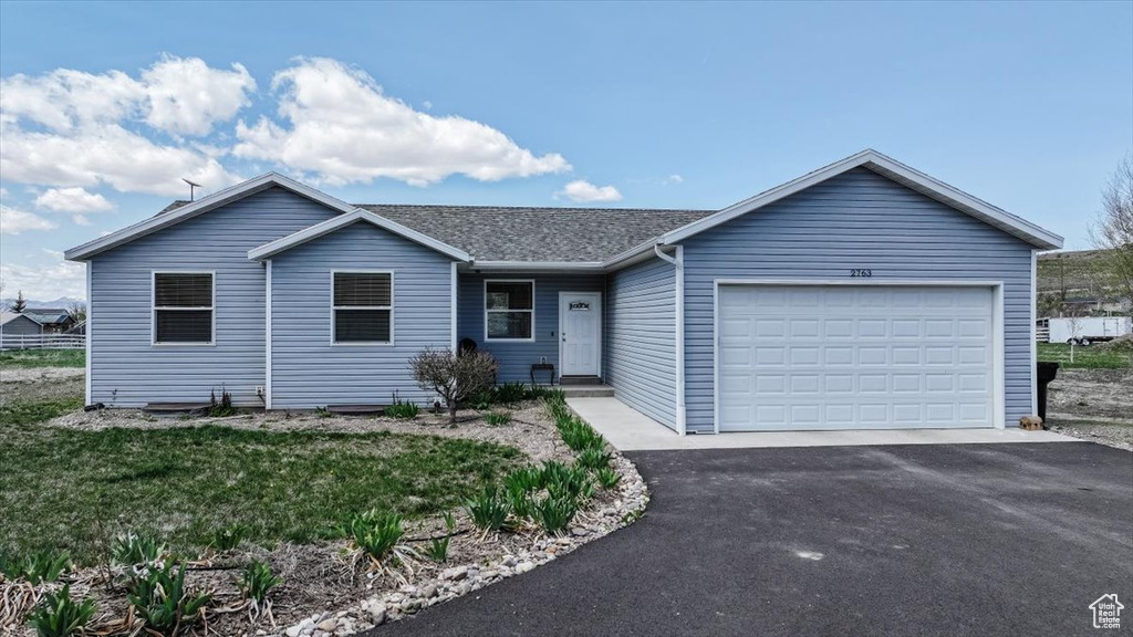 Single story home featuring an attached garage, a shingled roof, and driveway