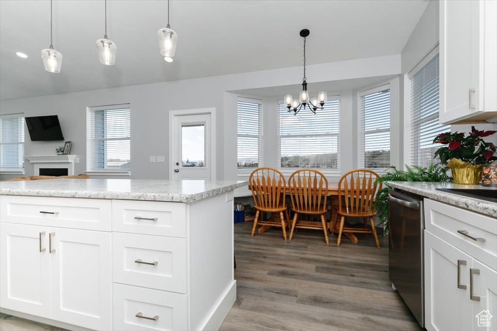 Kitchen with stainless steel dishwasher, light wood-type flooring, a fireplace, white cabinets, and a notable chandelier