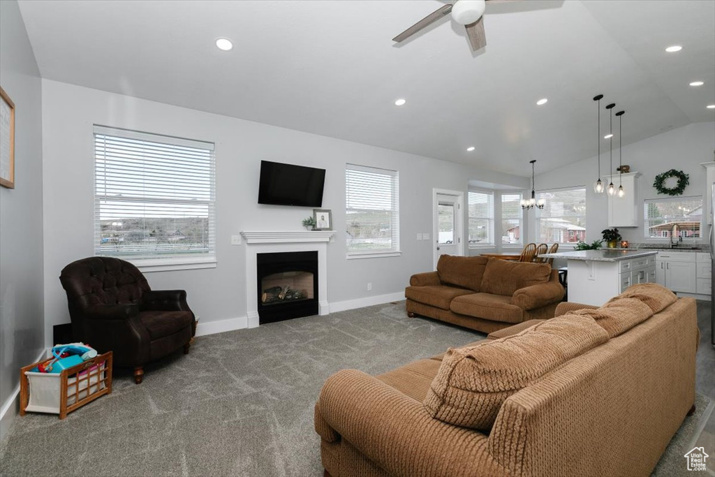 Carpeted living area with ceiling fan with notable chandelier, a fireplace, baseboards, lofted ceiling, and recessed lighting