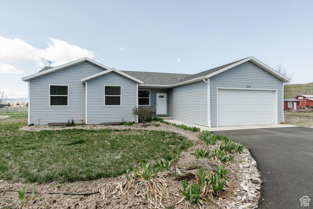 Single story home featuring an attached garage, aphalt driveway, roof with shingles, and a front yard