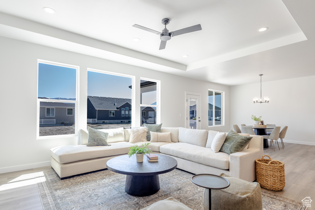 Living room with light wood-style floors, a chandelier, baseboards, a tray ceiling, and a ceiling fan