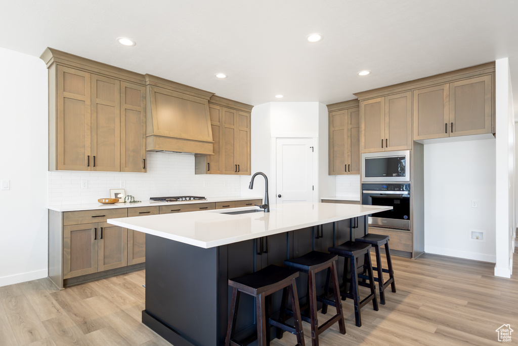 Kitchen featuring stainless steel appliances, custom exhaust hood, a sink, light wood-style floors, and recessed lighting