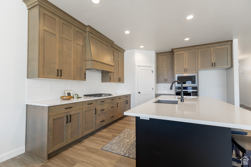 Kitchen with premium range hood, a sink, appliances with stainless steel finishes, decorative backsplash, and light wood-style floors
