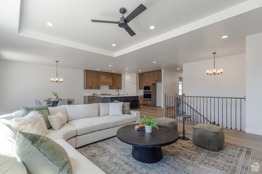 Living room featuring a chandelier, ceiling fan, light wood-style flooring, recessed lighting, and a tray ceiling
