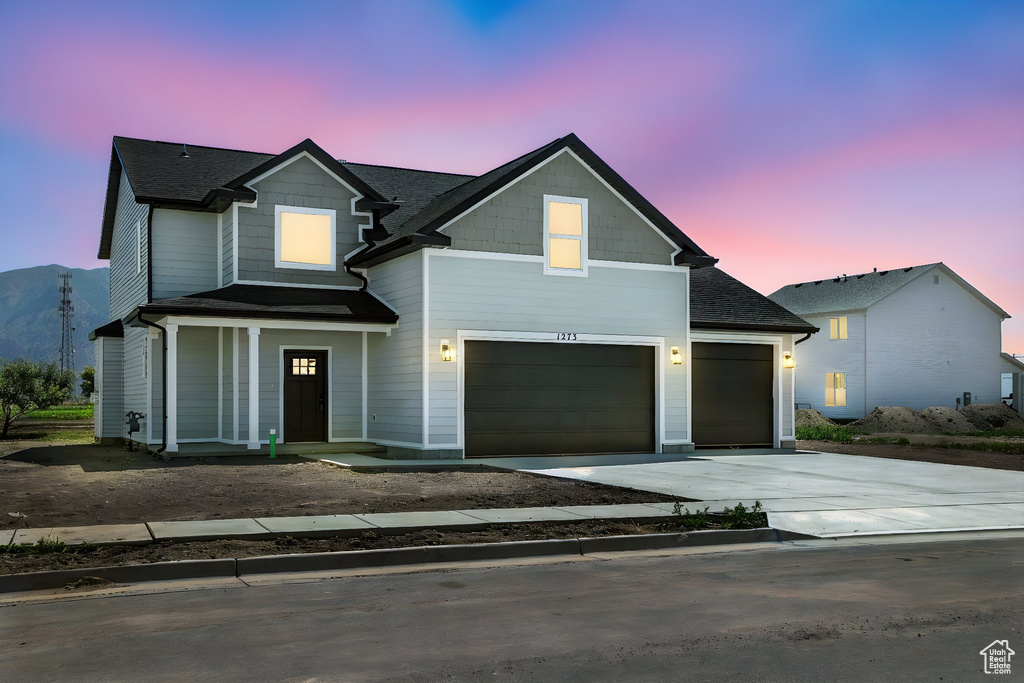 View of front of property featuring driveway, a garage, roof with shingles, and covered porch