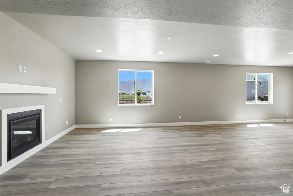 Unfurnished living room with wood finished floors, a glass covered fireplace, recessed lighting, and a textured ceiling