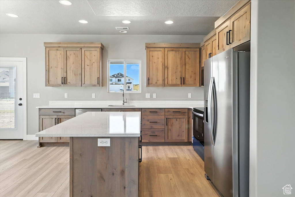 Kitchen featuring appliances with stainless steel finishes, recessed lighting, light wood finished floors, a center island, and a textured ceiling
