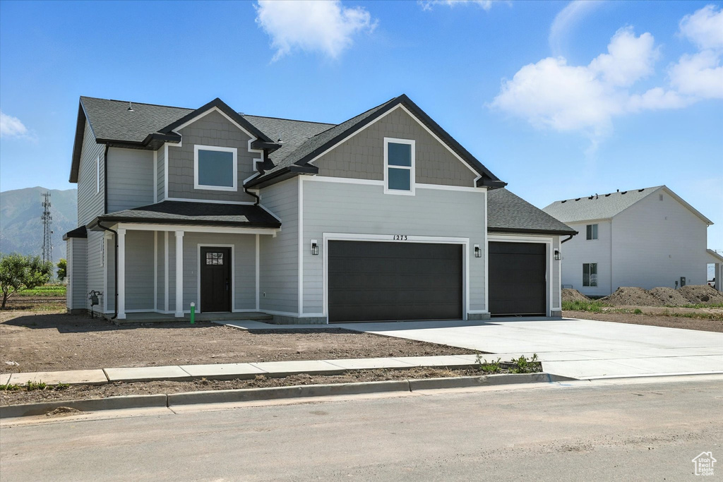 Craftsman-style home featuring concrete driveway, covered porch, an attached garage, and roof with shingles