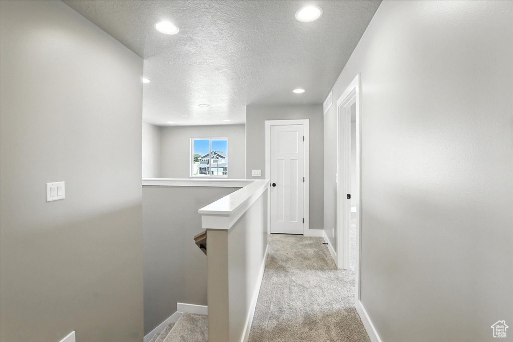 Corridor with an upstairs landing, a textured ceiling, light carpet, and recessed lighting