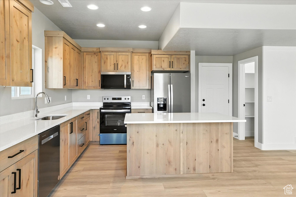 Kitchen featuring stainless steel appliances, light brown cabinetry, light wood-style floors, a kitchen island, and light countertops