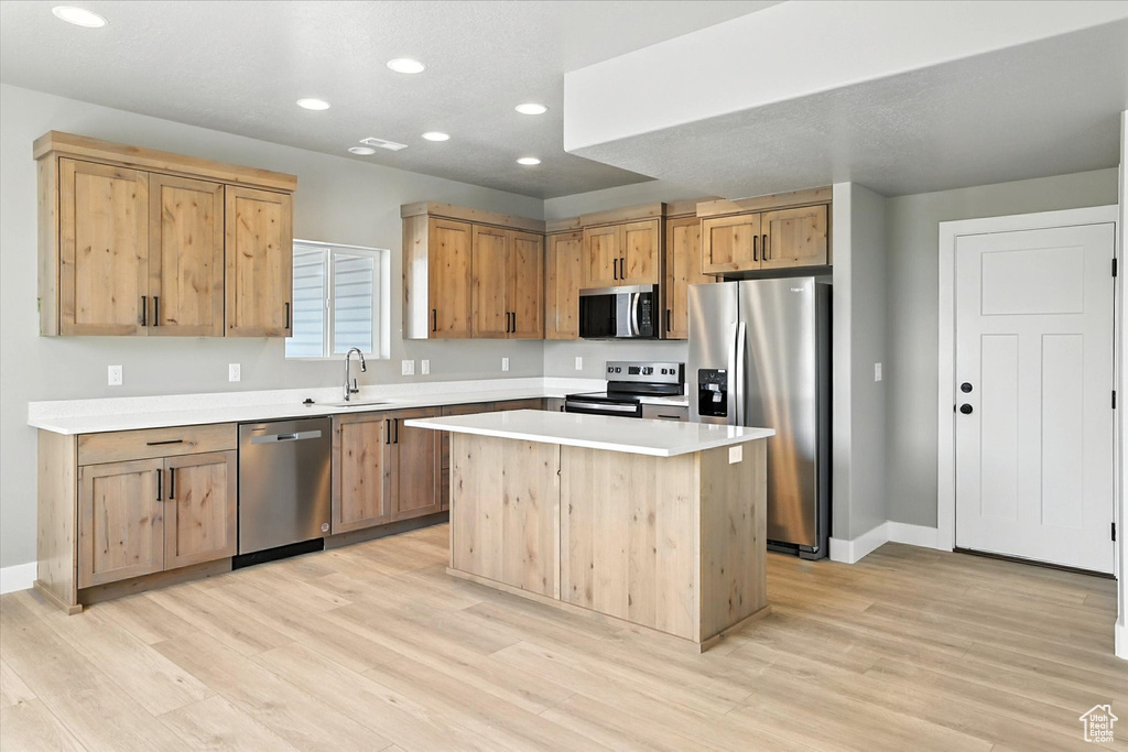 Kitchen featuring appliances with stainless steel finishes, recessed lighting, light wood finished floors, light countertops, and a center island