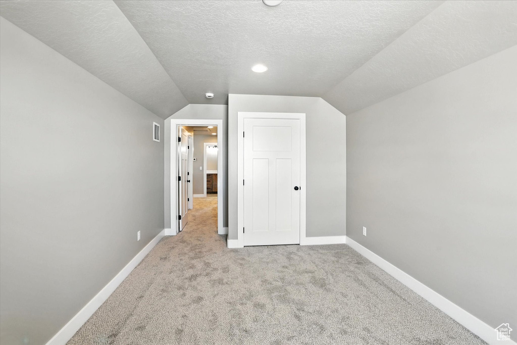 Unfurnished bedroom with carpet flooring, lofted ceiling, and a textured ceiling