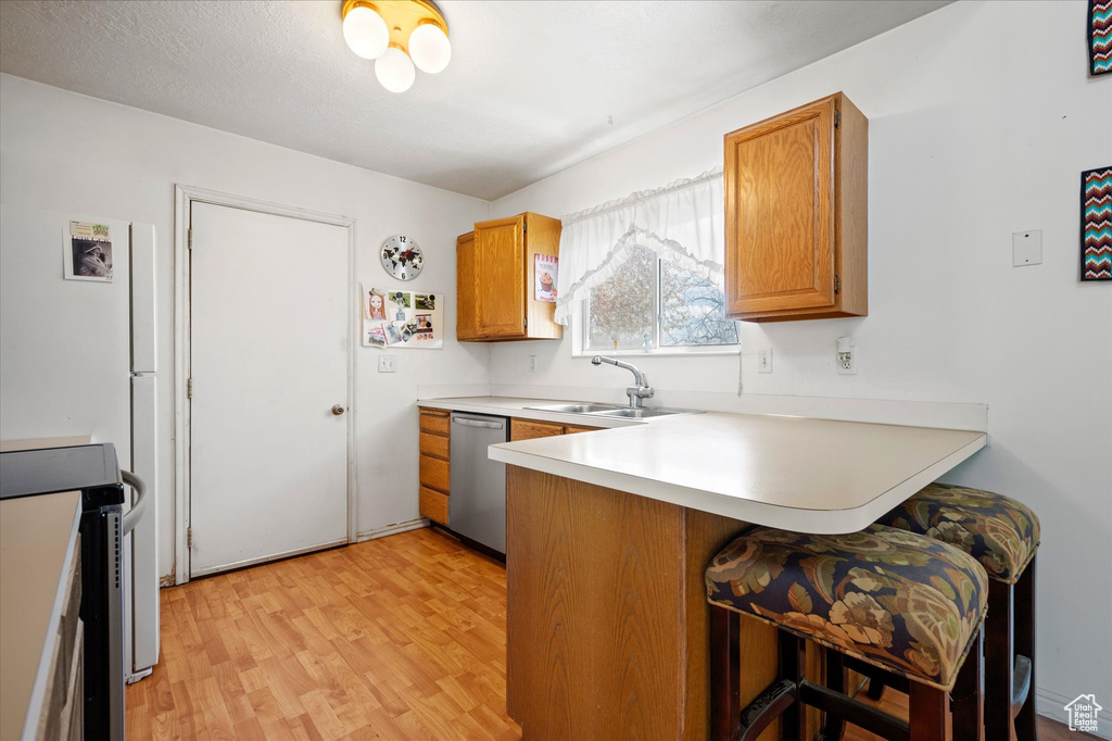 Kitchen with a kitchen breakfast bar, a sink, light wood finished floors, a peninsula, and appliances with stainless steel finishes