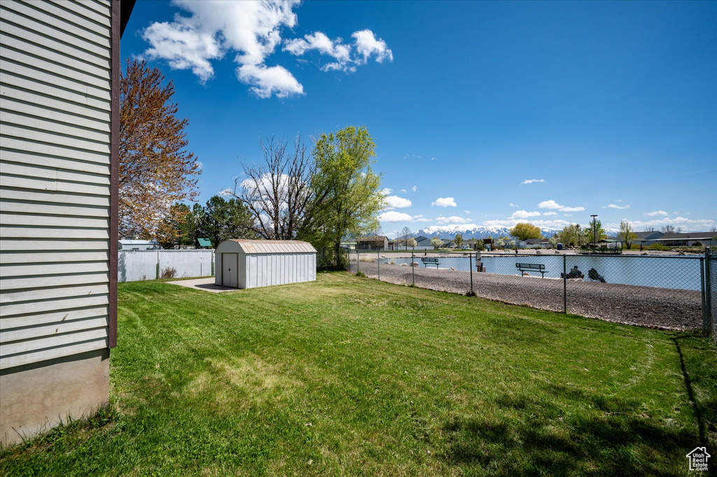 View of yard featuring a storage shed, a fenced backyard, a water view, and an outdoor structure