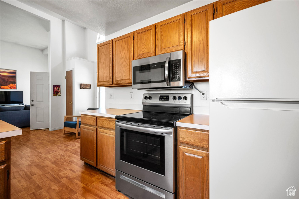 Kitchen featuring stainless steel appliances, light countertops, wood finished floors, and brown cabinets