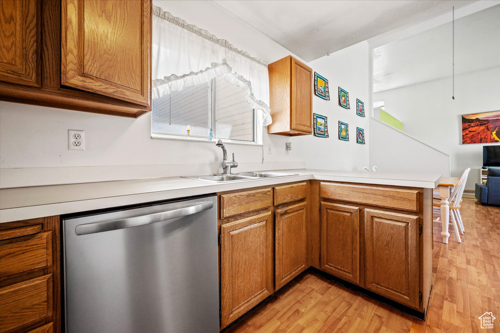 Kitchen with a peninsula, light countertops, a sink, light wood-type flooring, and dishwasher