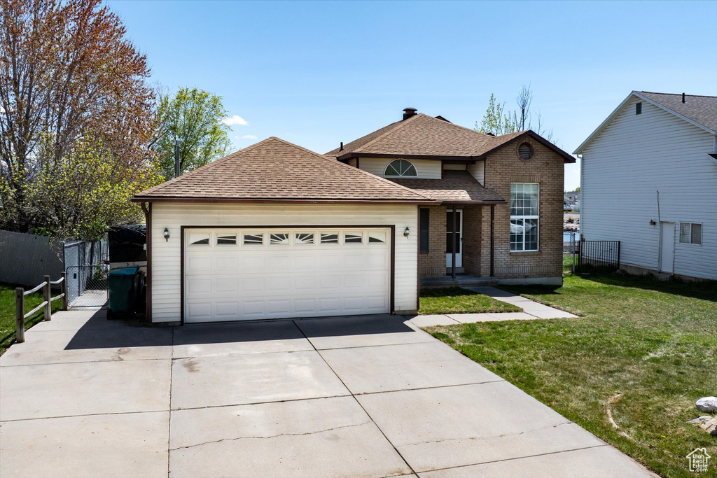 Traditional-style house featuring brick siding, concrete driveway, a front lawn, fence, and roof with shingles