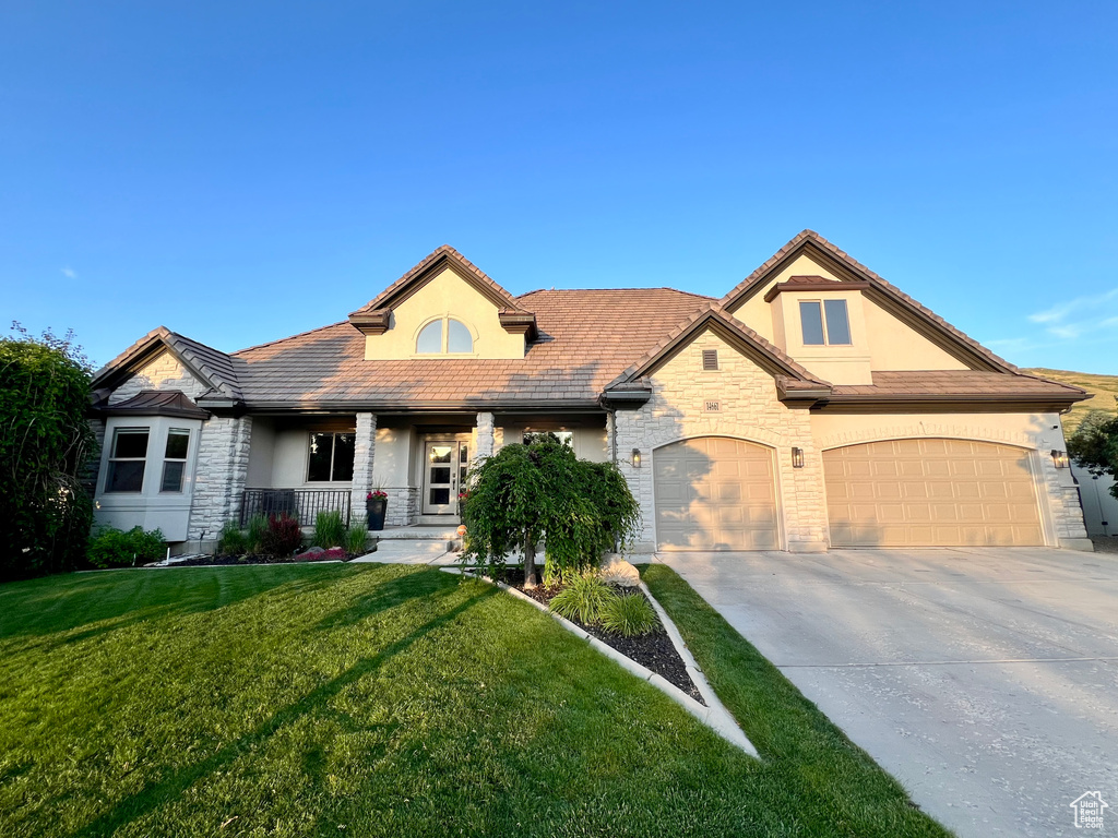 View of front facade with stone siding, stucco siding, a porch, driveway, and a front lawn