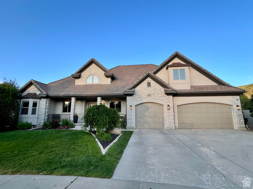French country style house featuring stucco siding, stone siding, concrete driveway, and a front yard