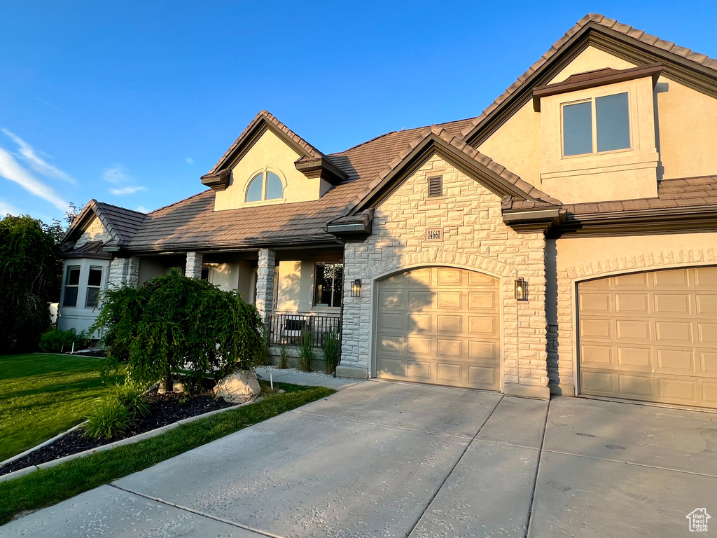 View of front facade featuring stone siding, concrete driveway, stucco siding, covered porch, and a garage
