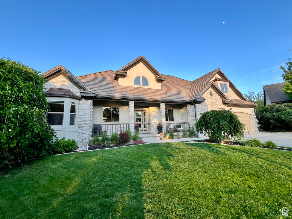 View of front of house with stone siding, covered porch, a front lawn, stucco siding, and a garage