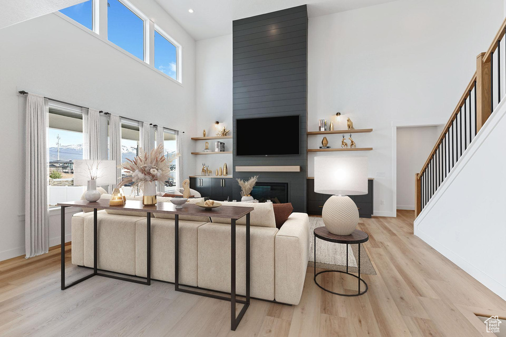 Living area featuring baseboards, a high ceiling, a large fireplace, and light wood-style flooring