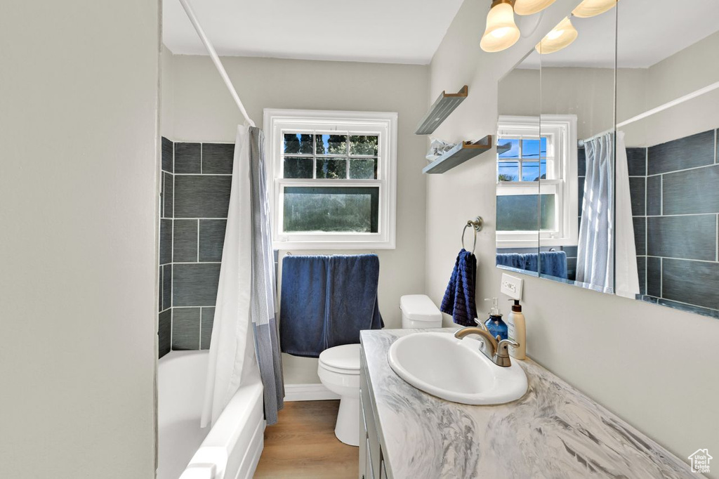 Full bathroom featuring wood finished floors, toilet, vanity, and shower / bath combination with curtain