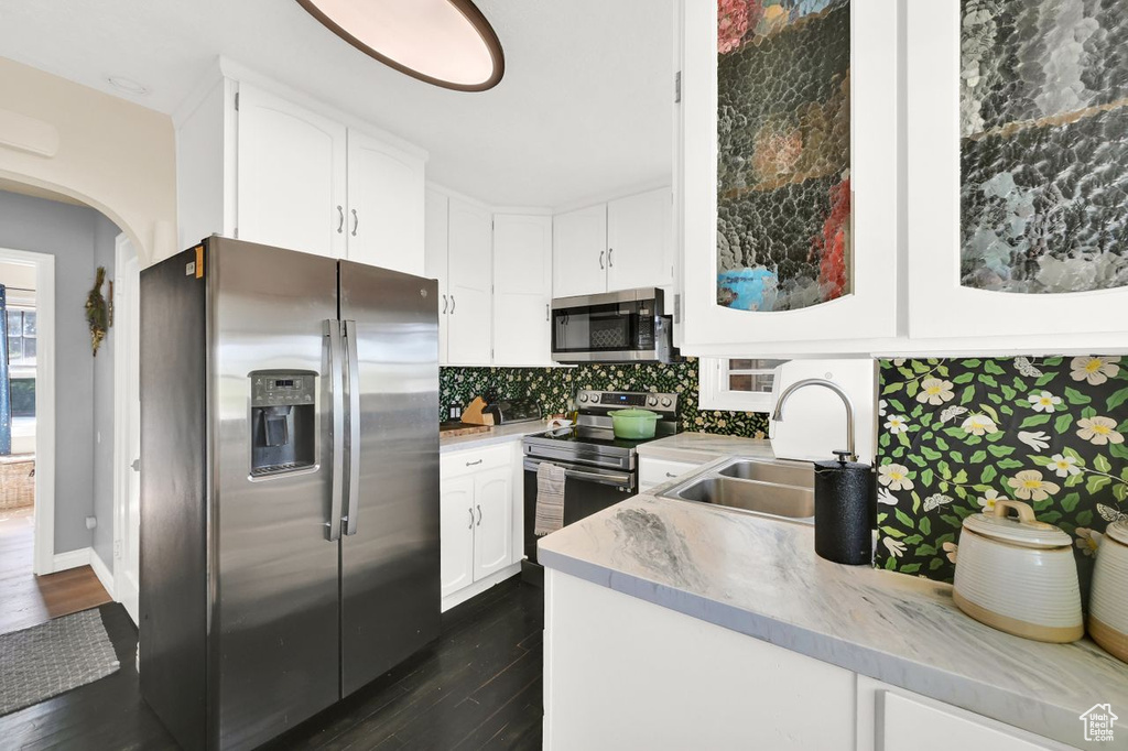 Kitchen featuring a sink, tasteful backsplash, dark wood finished floors, white cabinetry, and appliances with stainless steel finishes