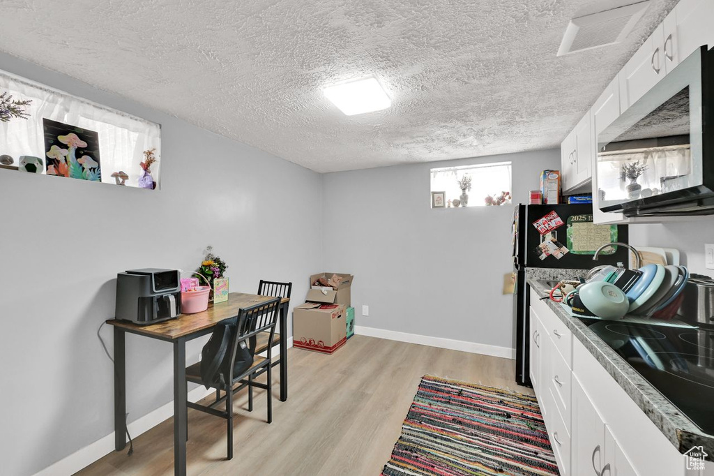 Kitchen featuring stainless steel microwave, light wood-style flooring, a textured ceiling, and white cabinets