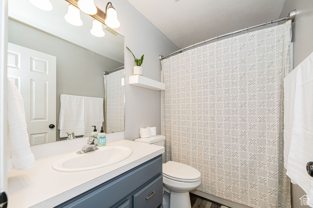 Bathroom with a shower with curtain, wood finished floors, vanity, and toilet