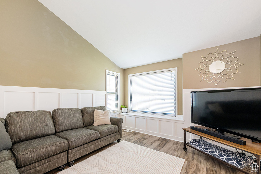 Living room with vaulted ceiling, wood finished floors, a decorative wall, and wainscoting