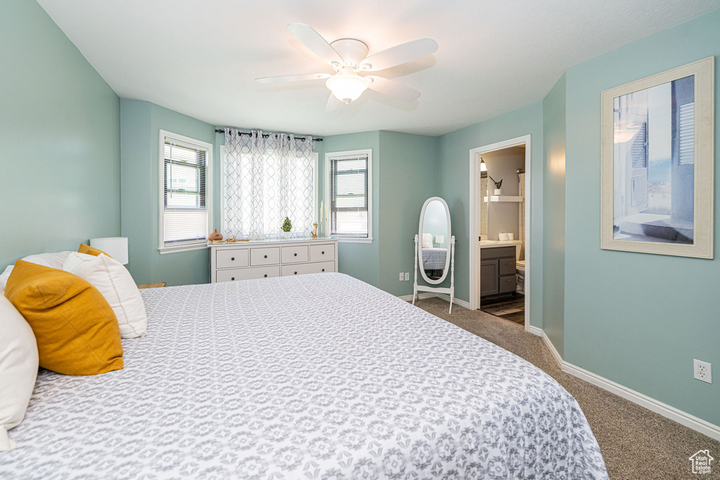 Bedroom featuring ensuite bath, dark colored carpet, baseboards, and multiple windows